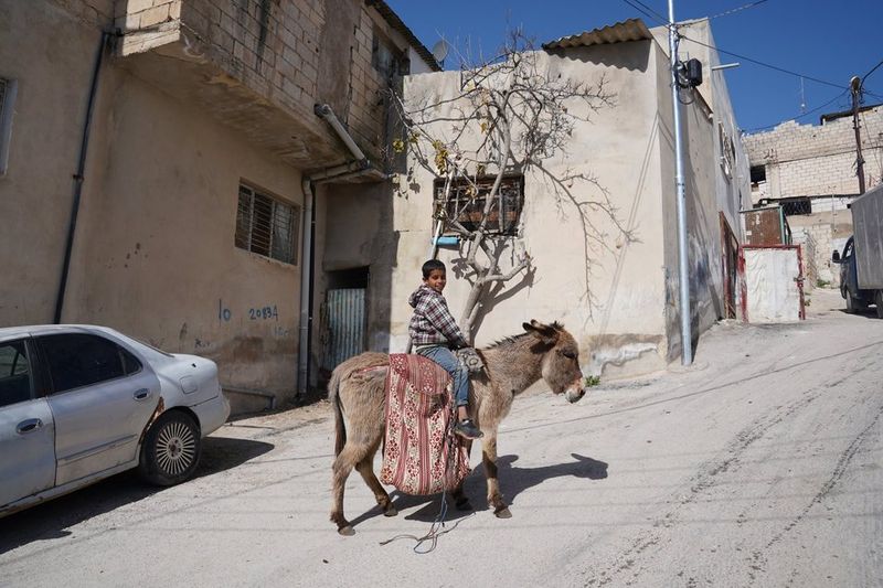 Still from Women in Exile: a boy riding a donkey up a street in the camp