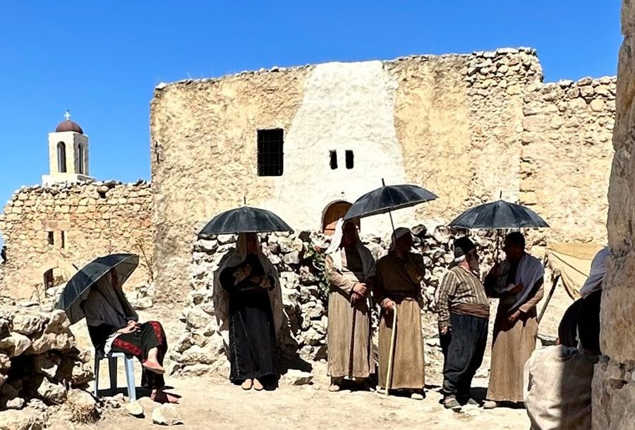 Behind the scenes on Palestine 36: actors in period costume under black umbrellas outside a stone village